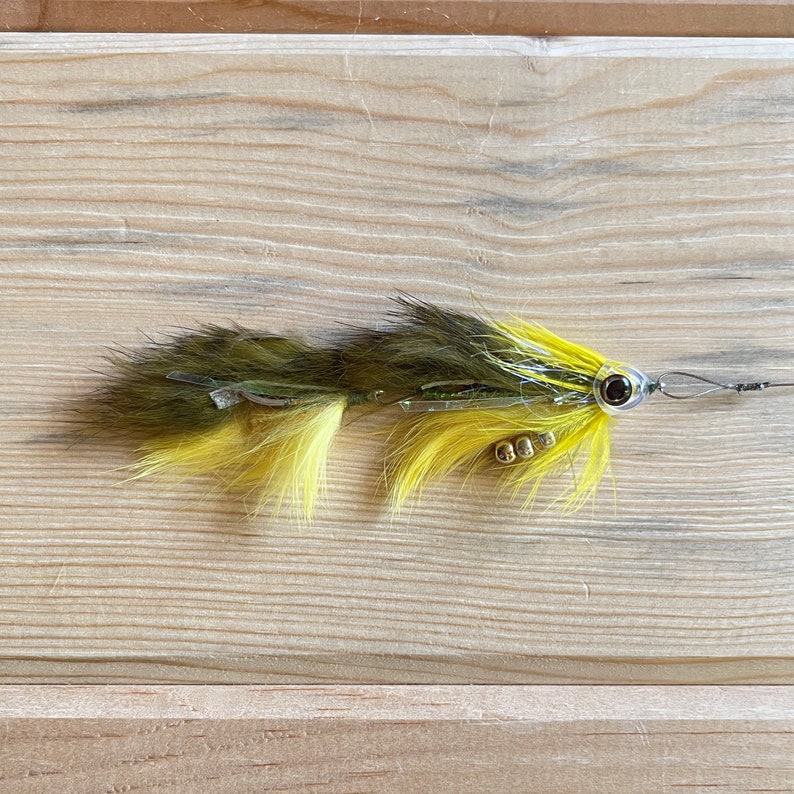 May include: A yellow and green fly fishing lure with a black eye and gold beads.