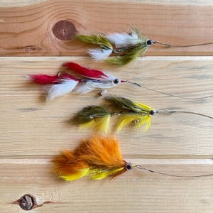 May include: Four fly fishing lures with different colored feathers and bodies. The lures are tied with green, red, yellow, and orange feathers.