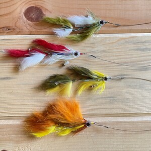 May include: Four fly fishing lures with different colored feathers and beads. The lures are arranged in a row on a wooden surface.