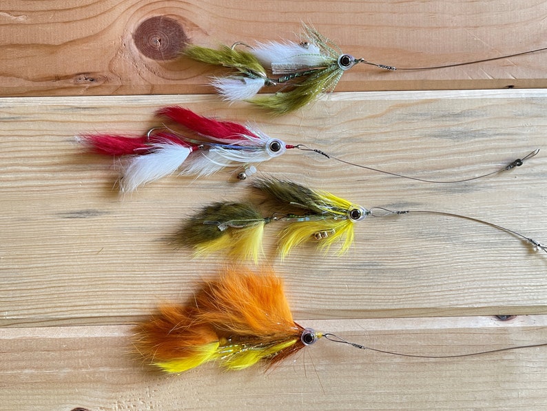 May include: Four fly fishing lures with different colored feathers and beads. The lures are arranged in a row on a wooden surface.