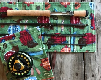 Puede incluir: Un rollo de tela verde con una caña de pescar y un carrete en su interior. La tela tiene un tema de campamento con imágenes de un camión rojo, una mochila y una canoa. El texto en la tela dice "No. 1 Campsite" y "The Great Outdoors".