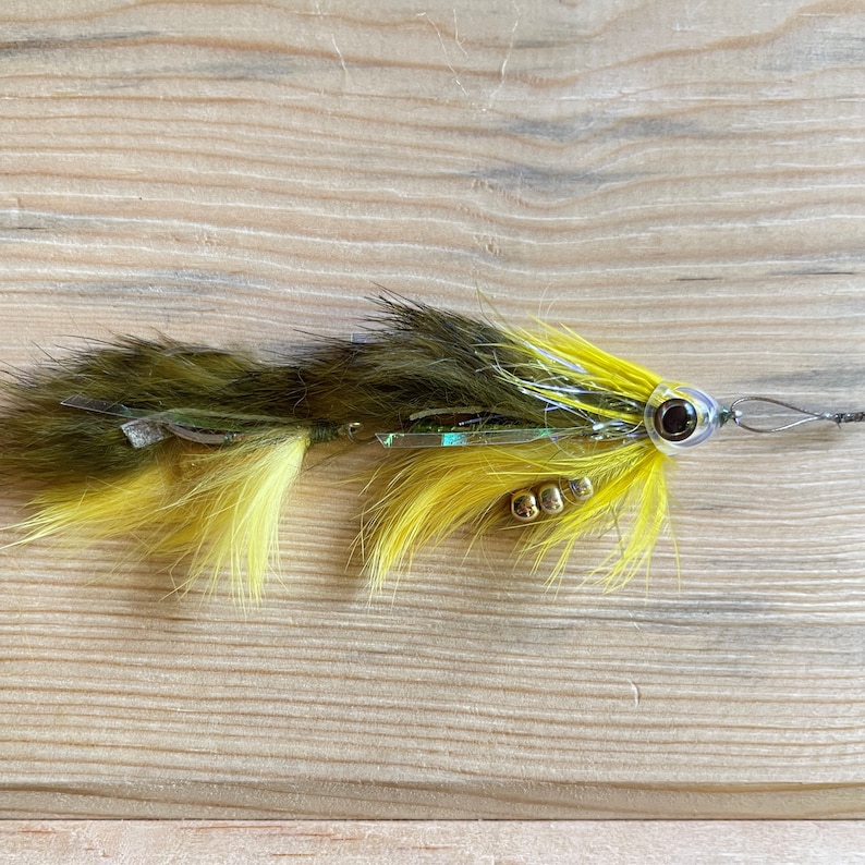 May include: A yellow and green fly fishing lure with a black eye and gold beads.