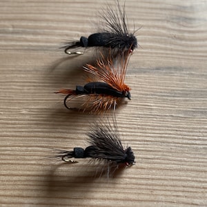 May include: Three black and orange fly fishing lures with black and orange feathers and a black foam body.