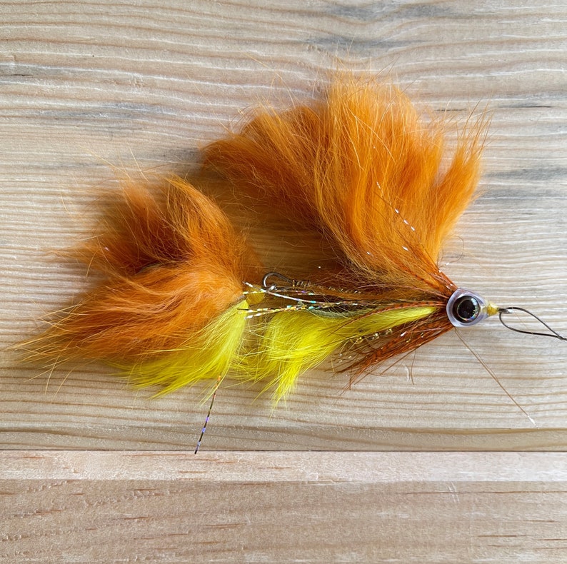 May include: A bright orange and yellow fly fishing lure with a black eye and a brown and silver body.