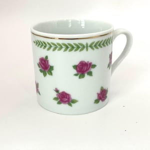 May include: White ceramic mug with a gold rim and handle. The mug is decorated with pink rose illustrations and a green leaf border. A classic design for enjoying hot beverages.