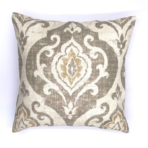 May include: A decorative throw pillow with a beige and gold damask pattern. The pillow has a square shape and a soft, textured fabric.