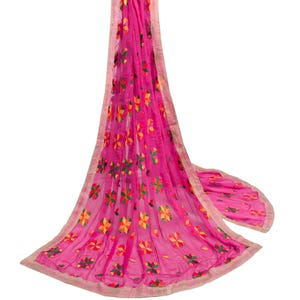 Peut inclure: Une écharpe rose vif avec des motifs floraux brodés en jaune, vert et rouge. L'écharpe a une texture délicate et transparente et une bordure dorée. Le motif floral est répété sur le tissu.