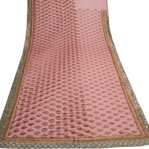 May include: A sheer, pale pink textile featuring a repeating pattern of brown leaf shapes. The edges are trimmed with a gold border and a green and gold patterned trim. The fabric is lightweight and appears to be draped.