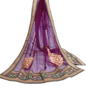 May include: A sheer, purple fabric with a decorative gold and green border. The border features floral embroidery and a gold trim. The fabric is draped over a stand, showcasing its delicate texture and design.
