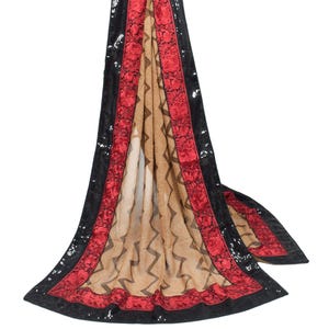 May include: A flowing scarf with a tan center featuring a zigzag pattern. The edges are trimmed with a red floral design and black sequined borders. The scarf is draped, showcasing its length and design.