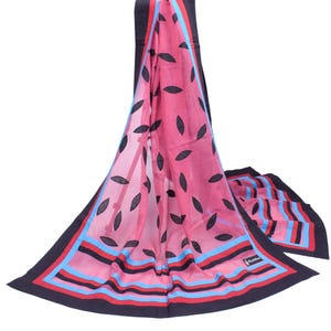 May include: A pink scarf with a black leaf pattern and a border of black, red, and blue stripes. The scarf is draped, showcasing its design and texture. The scarf is a fashion accessory.