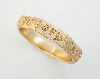 May include: A gold band ring with a decorative design featuring the letters "F" and "A" in a heart-shaped frame.