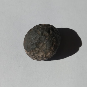 May include: A dark gray, round, textured rock with a rough surface.