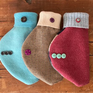 May include: Three different styles of dog sweaters with button closures. The sweaters are in shades of blue, brown, and red.