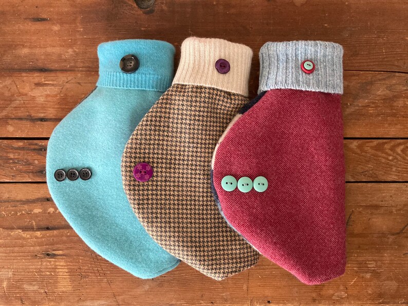 May include: Three different styles of dog sweaters with button closures. The sweaters are in shades of blue, brown, and red.