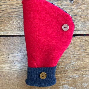 May include: Red fleece hand warmer with a navy blue cuff and two brown buttons. The hand warmer is folded in half and the cuff is visible.