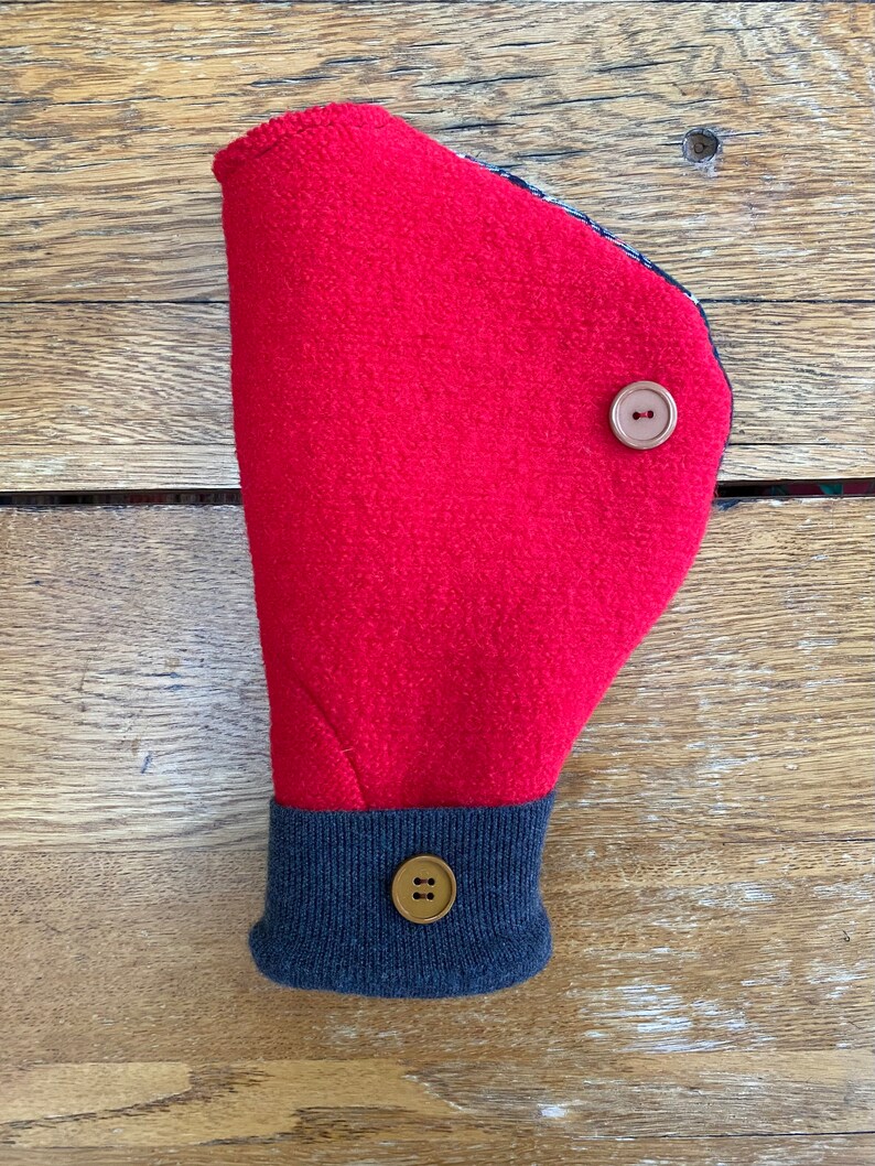 May include: Red fleece hand warmer with a navy blue cuff and two brown buttons. The hand warmer is folded in half and the cuff is visible.