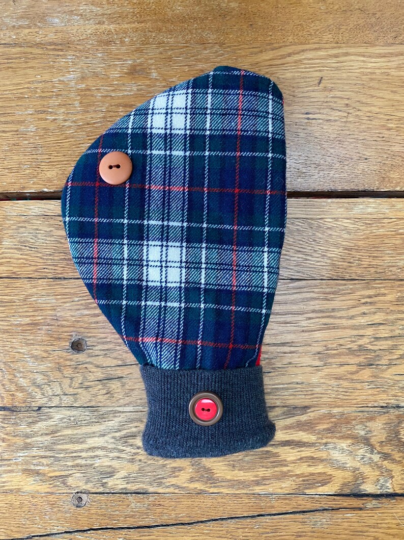 May include: A blue, green, red, and white plaid hand warmer with a gray cuff and two brown buttons. The hand warmer has a red button on the cuff.
