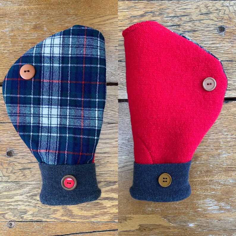 May include: Two hand warmers, one with a plaid pattern in shades of green, white, and red, and the other a solid red. Both have a gray cuff with a brown button.