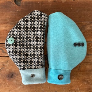 May include: Two hand warmers, one with a black and white checkered pattern and a light blue cuff, and the other a solid light blue with a light blue cuff. Both have black buttons.