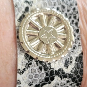 May include: A black and white snakeskin bracelet with a silver-toned star charm. The charm has a circular design with a star in the center.