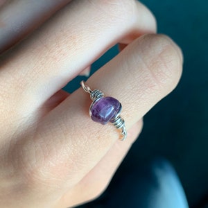 Può includere: Un anello avvolto in filo d'argento con una pietra di ametista viola.