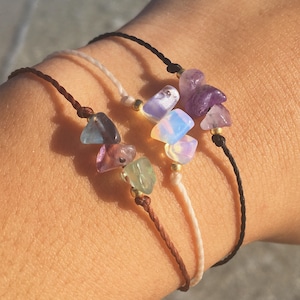 Peut inclure: Trois bracelets avec des cordons de couleurs différentes et des breloques en pierres précieuses. Les bracelets sont dotés d'un cordon marron, d'un cordon blanc et d'un cordon noir. Les breloques sont en améthyste, en opale et en fluorite.