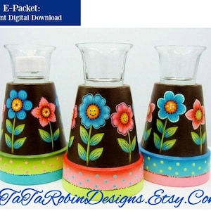 Könnte beinhalten: Drei braune Terrakotta-Blumentöpfe mit bemalten Blumen und grünen Blättern. Jeder Topf hat einen Glas-Votivhalter oben und ein buntes Punkteband unten herum.