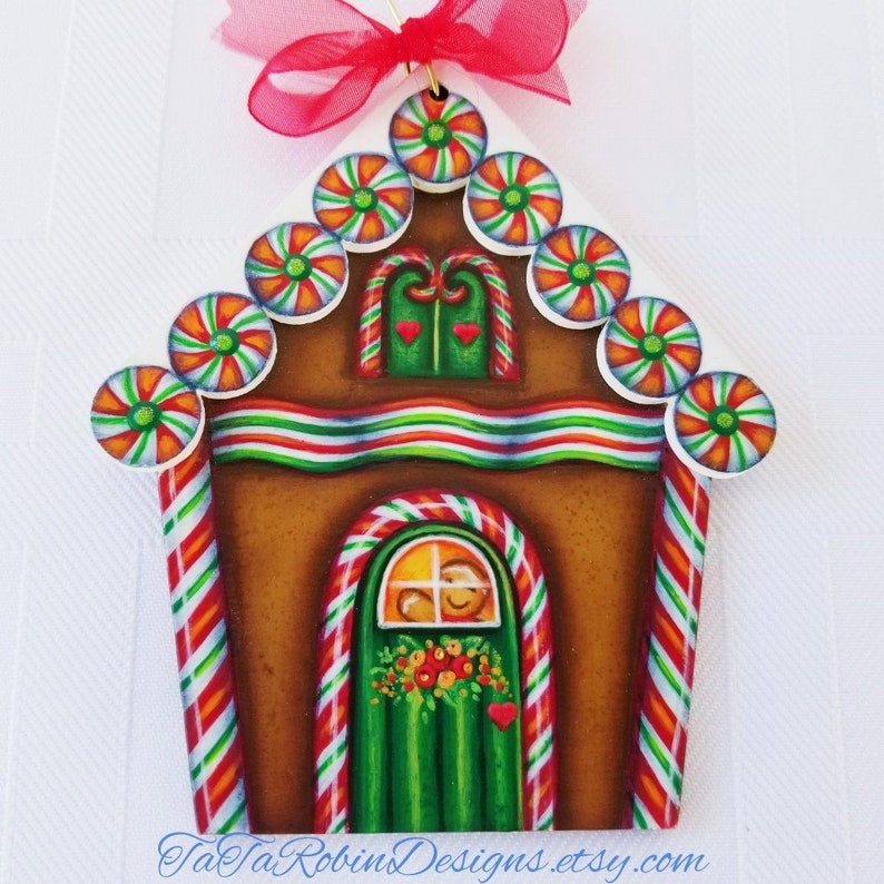 Peut inclure: Ornement de maison en pain d'&eacute;pices en bois peint &agrave; la main avec une bordure de b&acirc;ton de bonbon, des b&acirc;tons de bonbon ray&eacute;s rouge et blanc et une porte verte avec une couronne. Le toit est d&eacute;cor&eacute; de tourbillons de bonbons blancs, orange et verts.