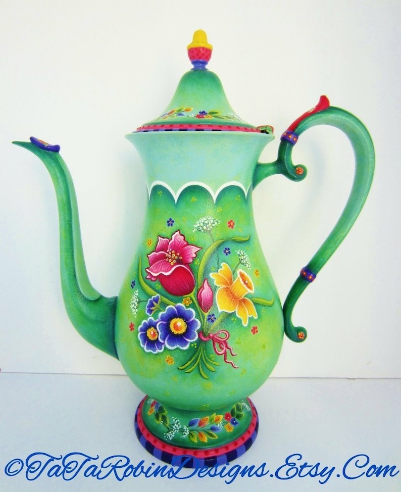 May include: A hand-painted green ceramic teapot with a floral design. The teapot has a scalloped edge and a floral design with pink, yellow, blue, and green flowers. The teapot has a black and white checkered base.
