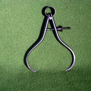 May include: A silver metal caliper with a round knob on the top and a small knob on the side. The caliper is open and ready to measure.