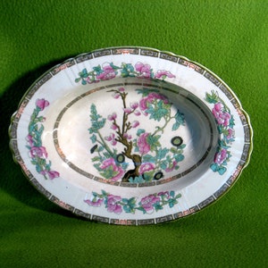 May include: A white oval serving dish with a floral pattern in shades of pink, green, and gold. The dish has a scalloped edge and a raised rim.
