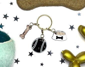May include: Gold key chain with three charms: a bone, a dog bowl, and a tennis ball. The charms are black and white with gold accents.