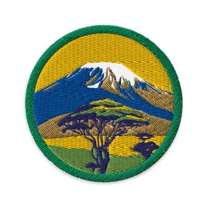 May include: Embroidered patch depicting a mountain scene with a tree. The patch has a yellow background and a green border. The mountain is blue and white, and the tree is green and yellow. The patch is circular.