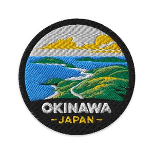 Könnte beinhalten: Gestickter Aufnäher mit einer Landschaft von Okinawa, Japan. Das Design zeigt blaues Meer, grüne Hügel, gelbe Wolken und den Text "OKINAWA - JAPAN" in Weiß und Gelb. Der Aufnäher hat einen schwarzen Rand und einen weißen Hintergrund.