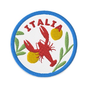 Könnte beinhalten: Runder, gestickter Aufnäher mit blauem Rand. Das Design zeigt das Wort "ITALIA" in Rot, einen roten Hummer, zwei gelbe Zitronen und grüne Blätter auf weißem Grund.