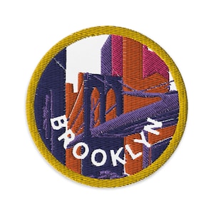May include: Embroidered patch featuring a Brooklyn cityscape with the Brooklyn Bridge. The design includes buildings in shades of orange, pink, and purple, with the word "BROOKLYN" in white. The patch has a gold border and a navy blue background.