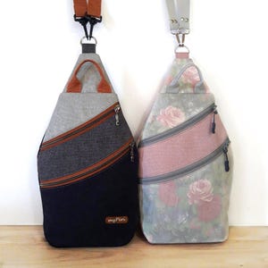 May include: Two sling bags with diagonal zippered pockets. One is gray, navy, and brown with a brown handle. The other is gray with pink stripes and a floral rose pattern. Both have adjustable straps and are displayed against a white background.