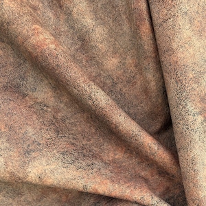 May include: Close-up of a textured fabric with a mottled appearance. The fabric features a blend of brown, rust, and black hues, creating a weathered, aged look. The material is folded, showing the texture and depth of the fabric.