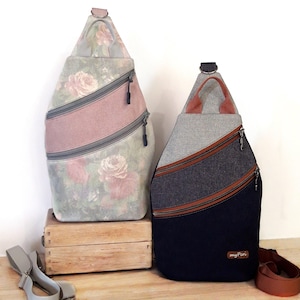 May include: Two sling backpacks. One features a floral rose pattern with a pink stripe and gray zippers. The other has a gray top, a dark blue bottom, and brown stripes with a brown strap.