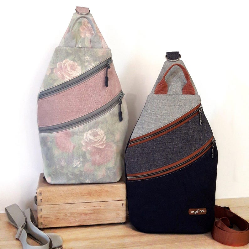May include: Two sling backpacks. One features a floral rose pattern with a pink stripe and gray zippers. The other has a gray top, a dark blue bottom, and brown stripes with a brown strap.