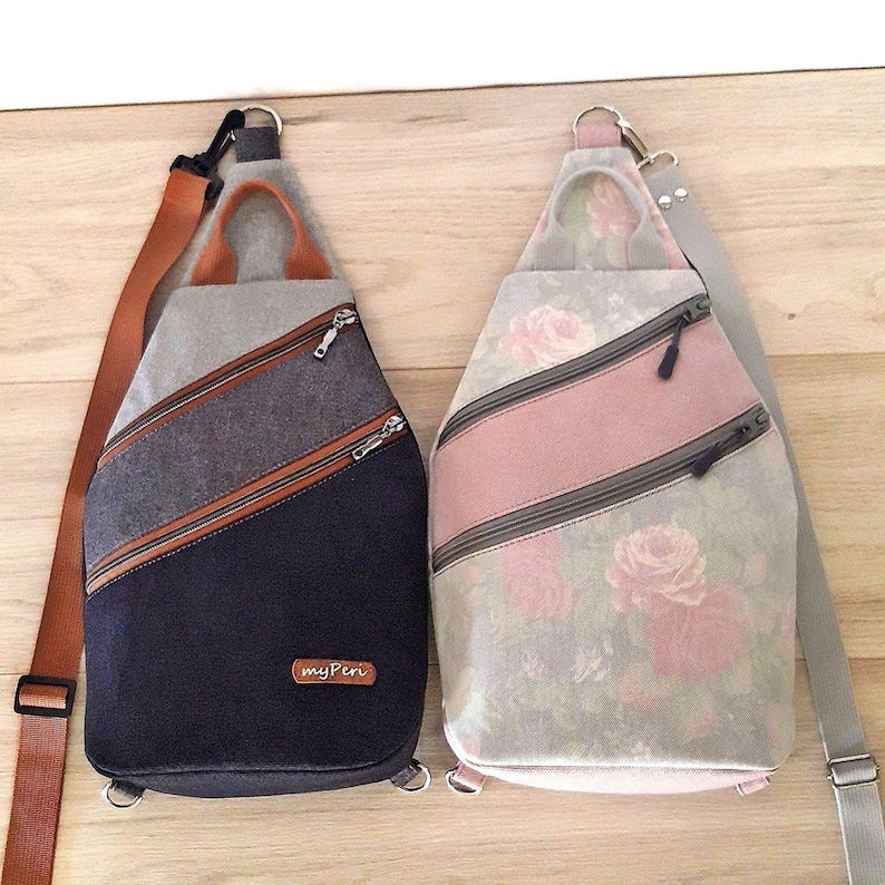 May include: Two sling bags with diagonal zippers. One is navy blue, gray, and brown. The other is light gray with pink roses and a pink stripe. Both have adjustable straps and top handles.