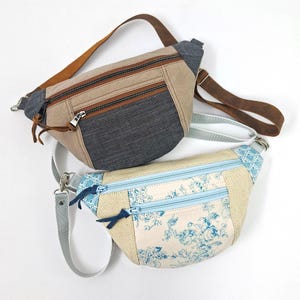 Könnte beinhalten: Zwei Bauchtaschen mit Reißverschlussfächern. Eine ist beige, Jeans und braunes Leder. Die andere ist hellblau, mit Blumendruck und beige. Beide haben verstellbare Riemen und silberfarbene Hardware.
