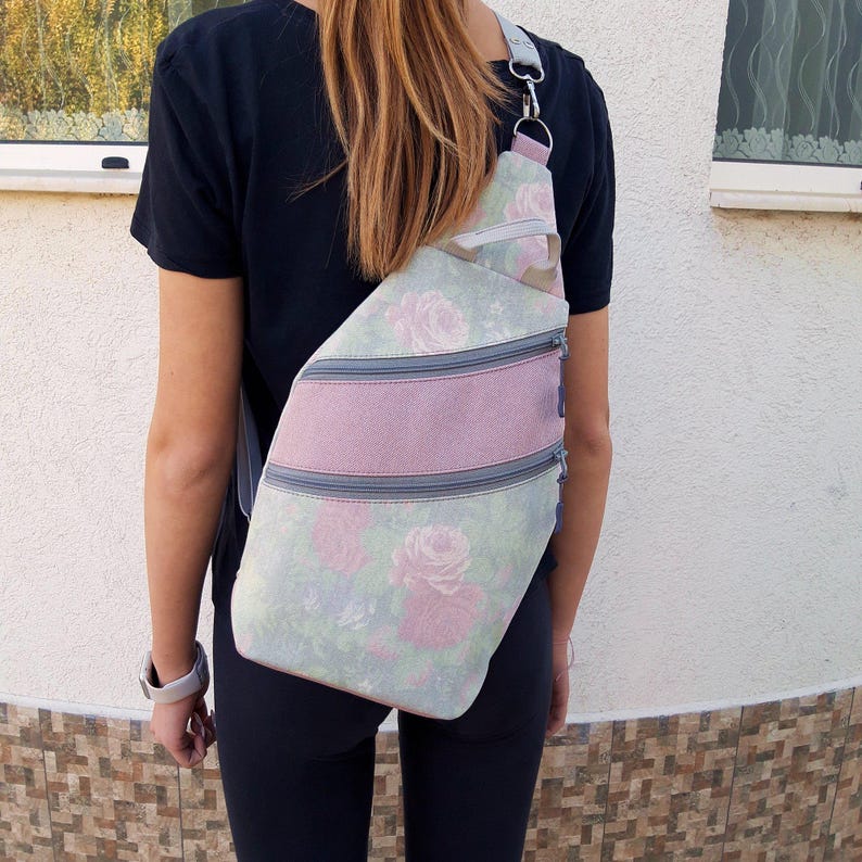 May include: A floral print sling bag with a pink stripe and three zippered compartments. The bag features a light green background with pink roses and a gray strap.
