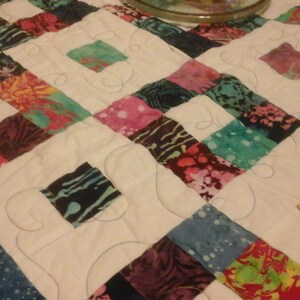 May include: A white quilt with a patchwork design featuring squares of various colorful fabrics. The quilt is quilted with a decorative swirl pattern.