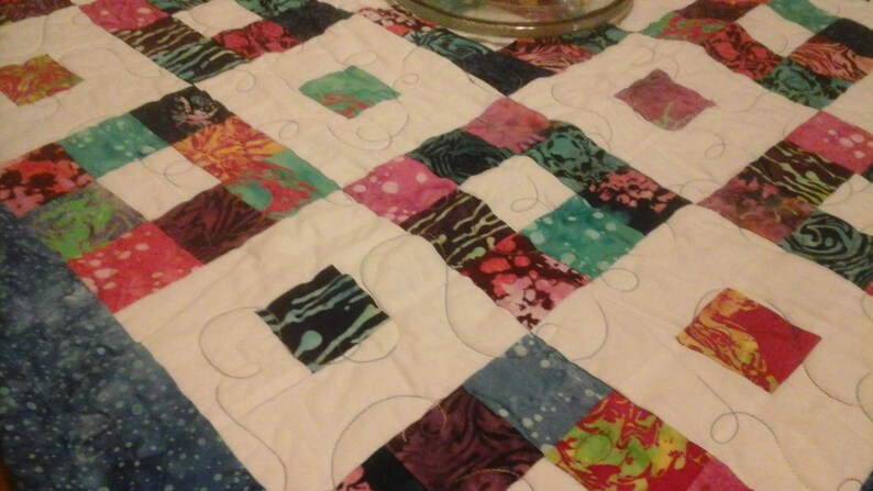 May include: A white quilt with a patchwork design featuring squares of various colorful fabrics. The quilt is quilted with a decorative swirl pattern.
