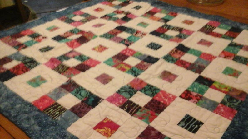 May include: A white quilt with a blue border. The quilt is made of squares of different fabrics, each with a unique pattern. The fabrics are mostly shades of blue, green, and purple.
