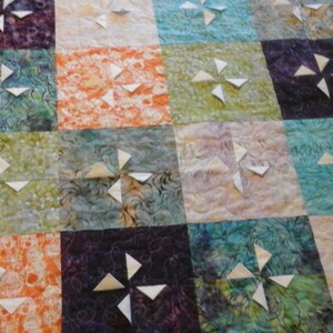 May include: A patchwork quilt with a variety of colorful fabrics and white fabric triangles sewn on top. The quilt is made up of 12 squares.