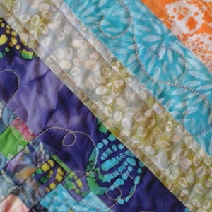 May include: A colorful patchwork quilt with a variety of fabrics and patterns, including floral, geometric, and abstract designs. The quilt is stitched together with white thread and has a quilted texture.