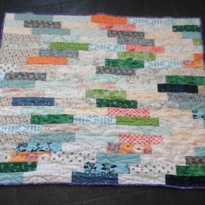 May include: A patchwork quilt with a variety of colorful fabrics, including green, blue, orange, and pink. The quilt is made up of many different squares and rectangles, and it has a white background.
